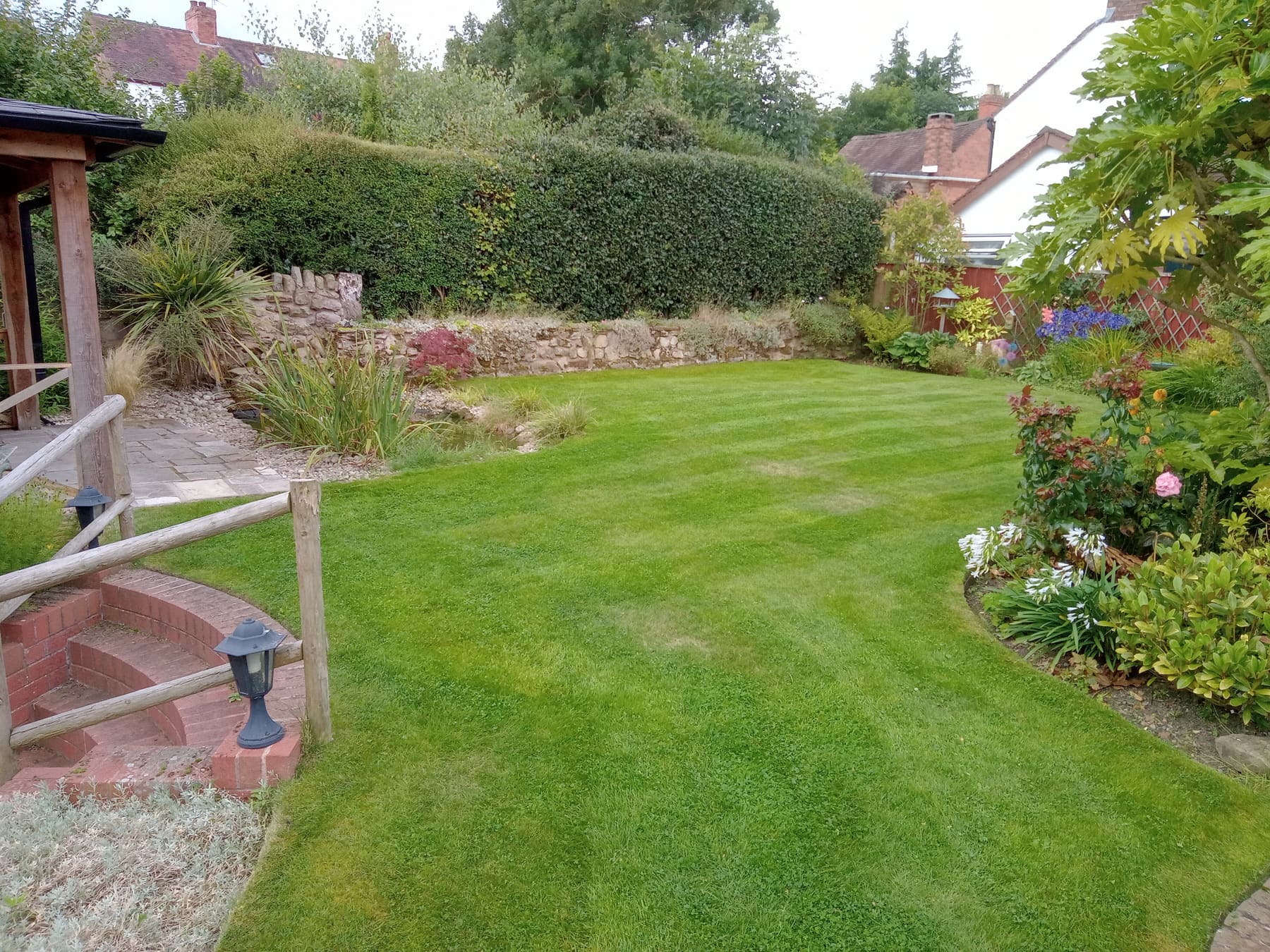 Well-kept garden lawn edged around a pond and flower borders
